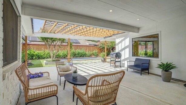 Un patio cubierto con mobiliario de mimbre, una parrilla y vistas a un jardín.