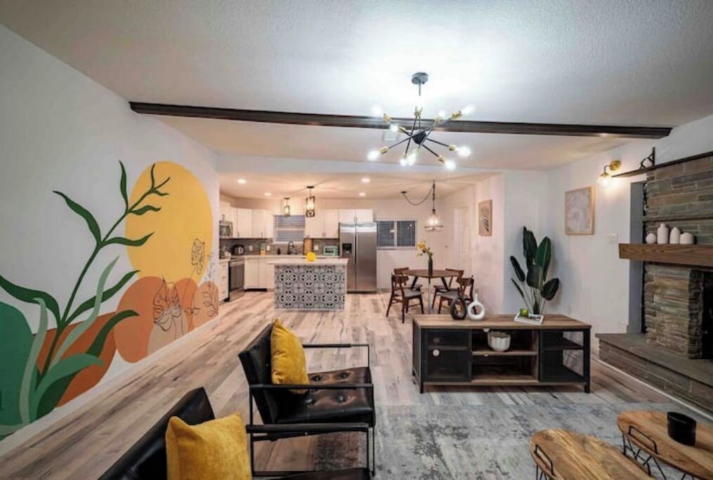 A modern living room with a sofa, coffee table, and chairs. There is a kitchen in the background with a dining area.