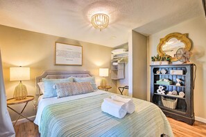 A neatly arranged bedroom with a bed, bedside lamps, a chandelier, a mirror, and a shelf with decorative items. - Rooftop Deck + Lake Cabin w/ Swim-Dock (Willis)