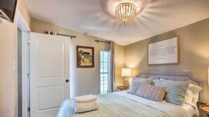 A bedroom with a bed, a bedside table with a lamp, a framed quote on the wall, and a door. - Rooftop Deck + Lake Cabin w/ Swim-Dock (Willis)