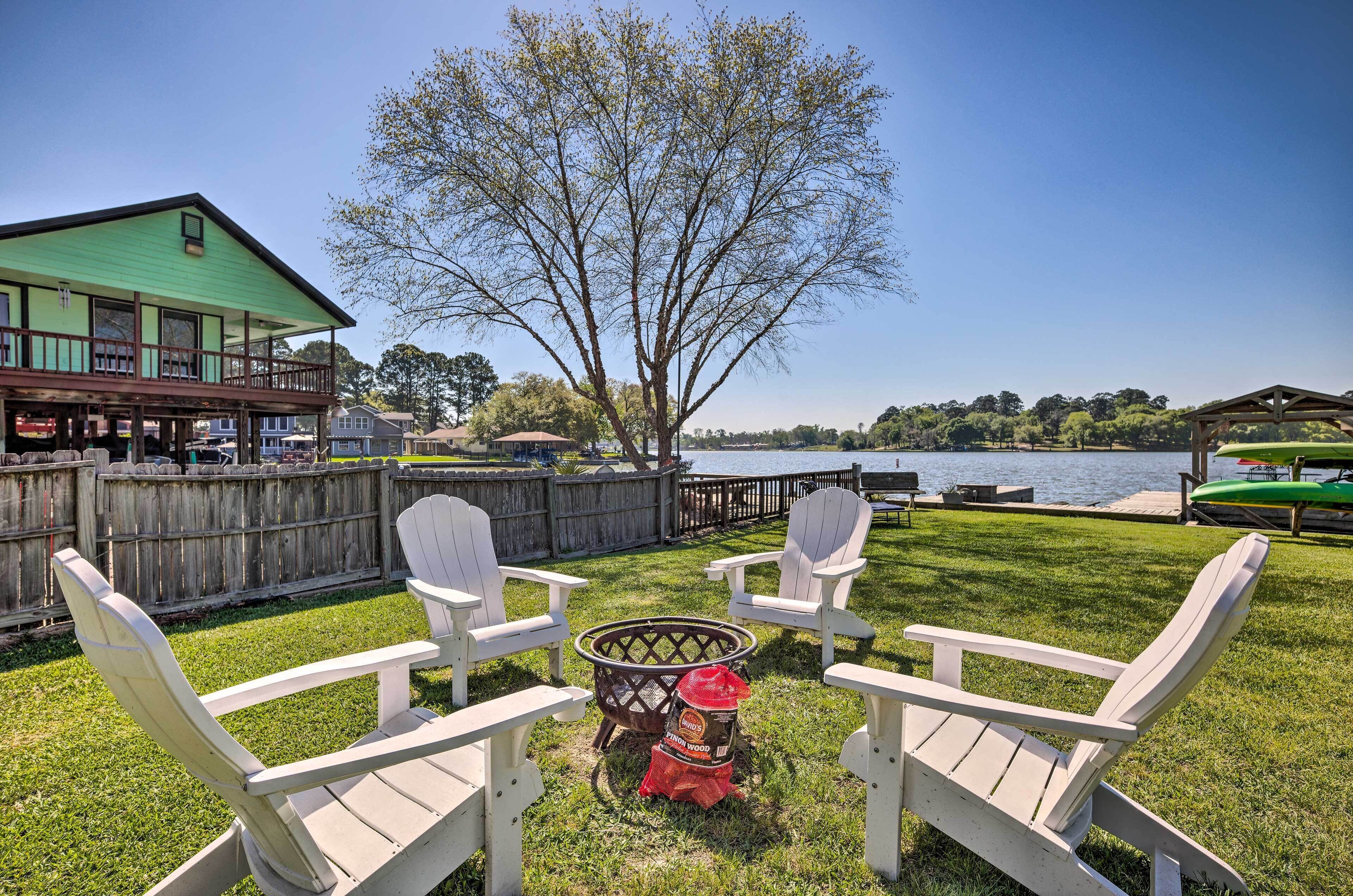 A backyard with a fire pit, Adirondack chairs, and a view of a lake.