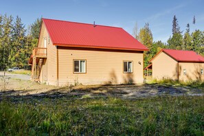 Una cabaña de madera de dos pisos con techo rojo, ubicada en un área boscosa.