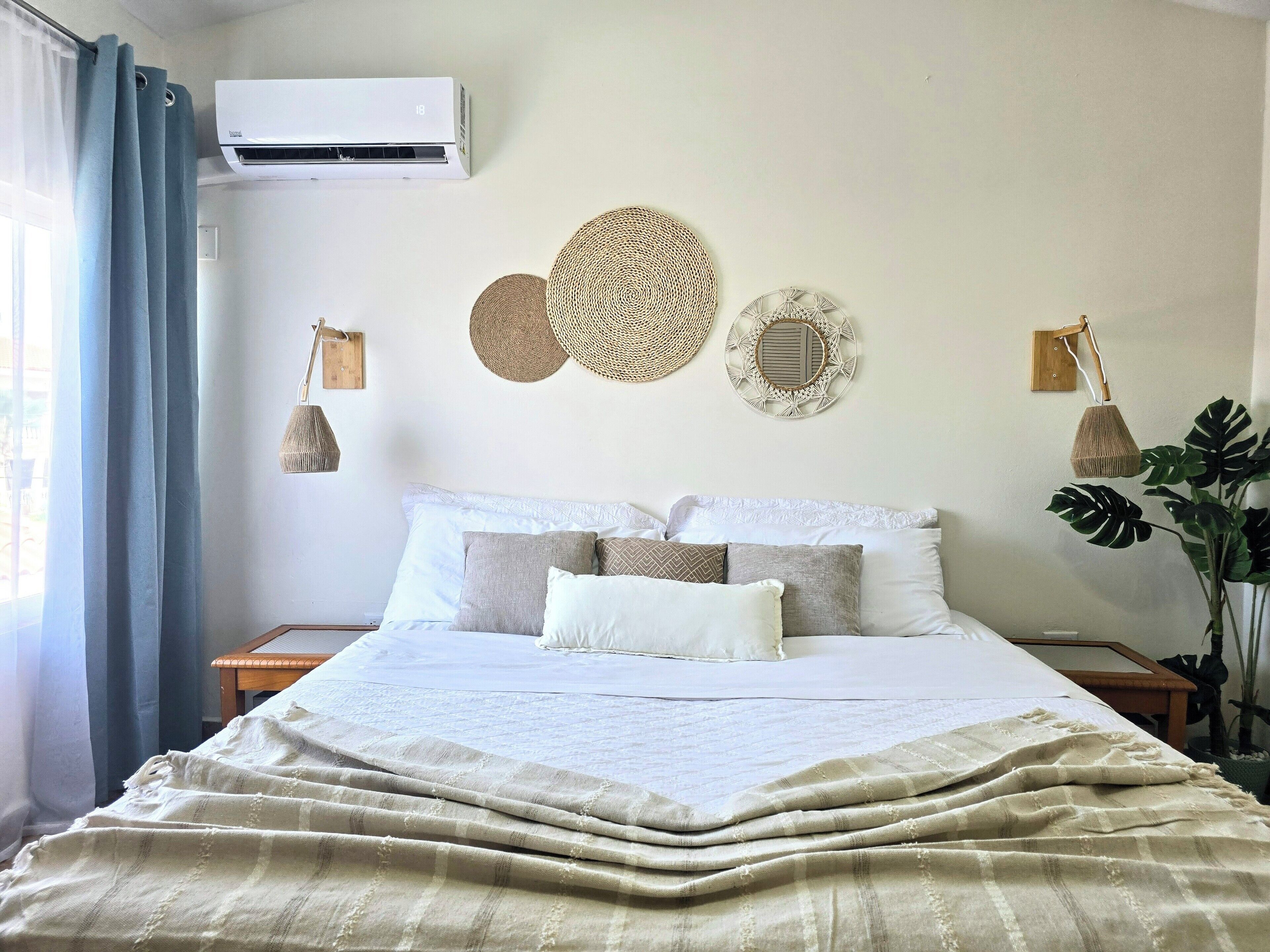 Uma cama bem arrumada com um cobertor listrado, um ar condicionado fixado na parede e duas luminárias também fixadas na parede.