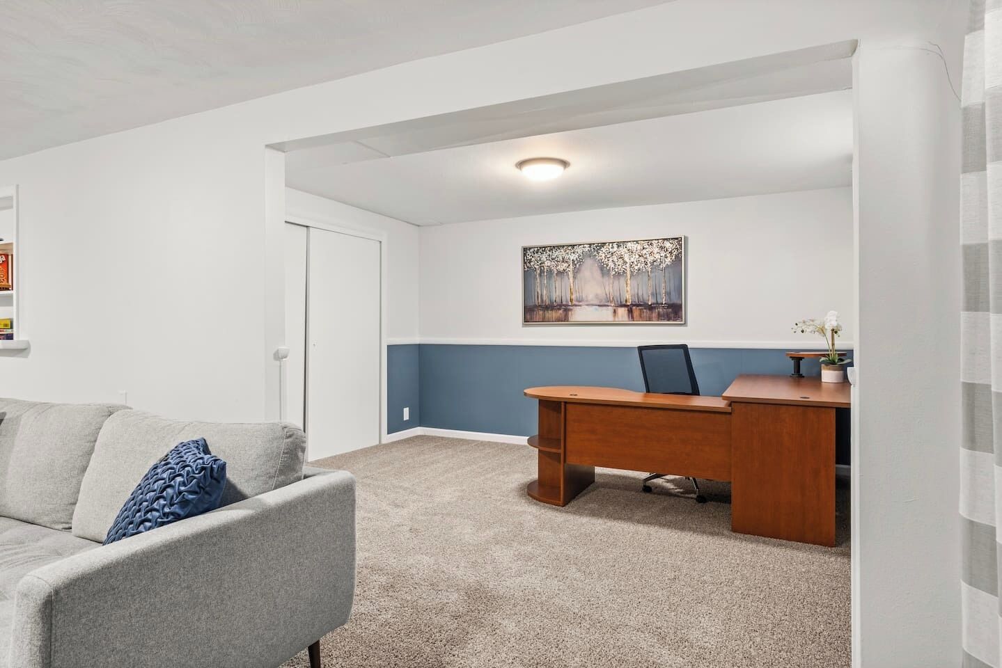 A room with a desk, a chair, a couch, a door, and a painting on the wall.