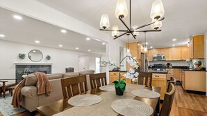 A modern kitchen with wooden cabinets, a dining area with a wooden table and chairs, and a living room with a sofa and a fireplace. - Spectacular Mountain Views - Hot Tub & Fire Pit (Centennial)