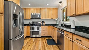 A kitchen with wooden cabinets, stainless steel appliances, a black countertop, and a window. - Spectacular Mountain Views - Hot Tub & Fire Pit (Centennial)