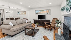 A living room with a sofa, coffee table, TV, fireplace, and a dining area with chairs and a table. - Spectacular Mountain Views - Hot Tub & Fire Pit (Centennial)