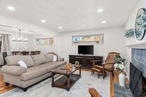 A living room with a sofa, coffee table, TV, fireplace, and a dining area with chairs and a table.