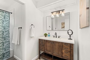 A bathroom with a white vanity, wooden cabinet, and a large mirror with lights.