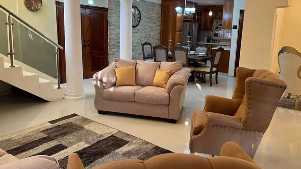 Un salon spacieux avec un canapé, des fauteuils, un lustre et un escalier.