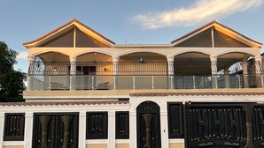 Un immeuble à plusieurs étages doté d’un balcon, de grandes fenêtres et d’une entrée fermée par un portail.
