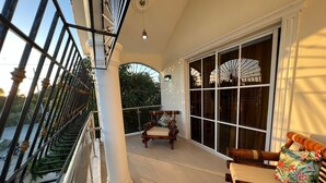 Un balcon avec un banc en bois, une chaise et une grande fenêtre avec un ventilateur.