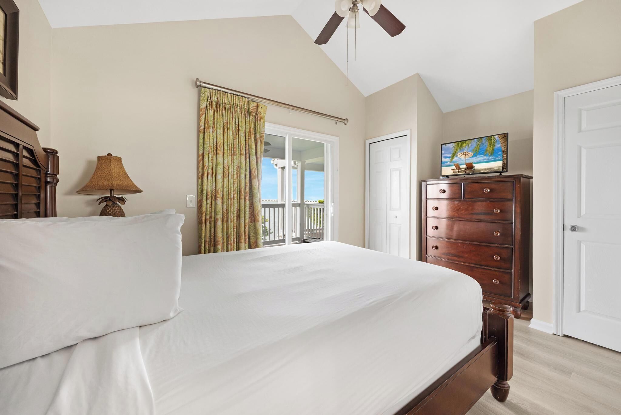 A bedroom with a bed, a dresser, a ceiling fan, a window with curtains, and a door.