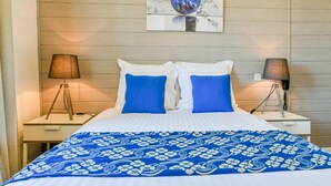 Una habitación de hotel con cama, dos lámparas de noche, una obra de arte en la pared y una colcha azul con estampado floral.
