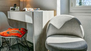 A modern room with a white console table, a grey upholstered chair, and a vibrant orange cushion. - Logis Hostellerie du Neez (Gan)