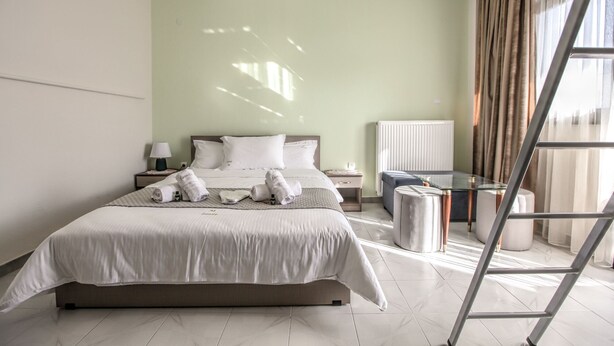 Quarto de hotel moderno com uma cama grande, uma mesa de cabeceira com abajur, uma mesa de vidro e uma escada.