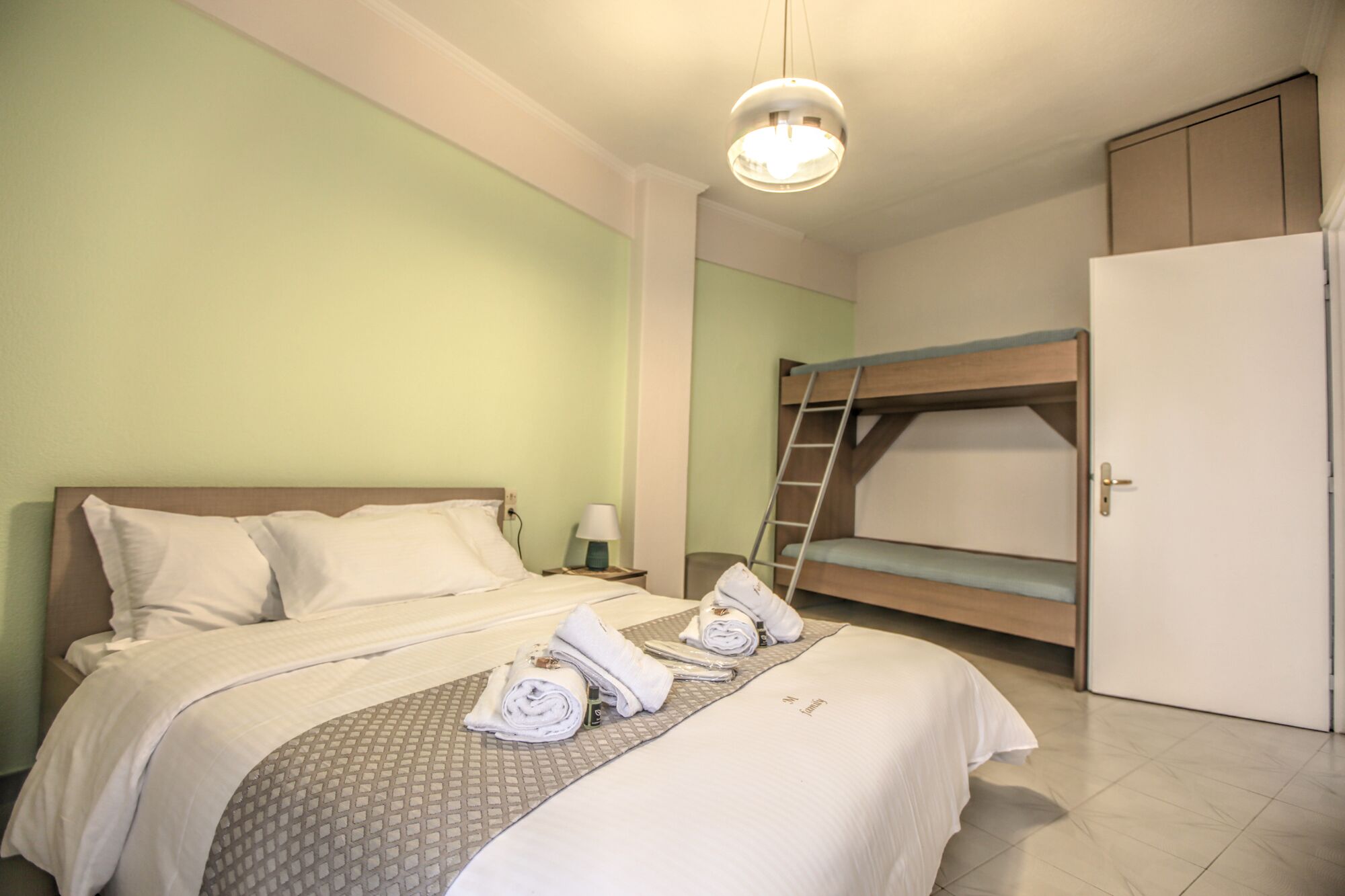 A hotel room with a single bed, a bunk bed, a wardrobe, and a bedside table with a lamp.