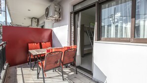 Uma varanda com mesa e cadeiras, uma divisória vermelha e uma porta de vidro deslizante que dá para uma escadaria.