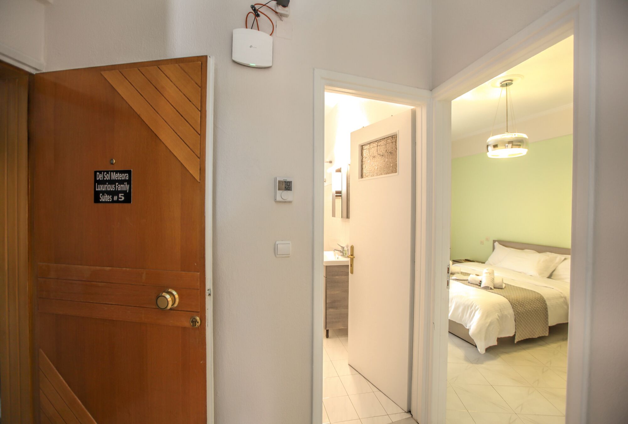 A hotel room with a bed, a bedside table, and a nightstand. There is a door with a sign indicating the room number and type.