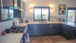 A modern kitchen with dark cabinetry, a gas stove, and a large window providing a view of the outdoors.