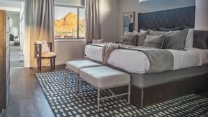 A modern bedroom with a large bed, a bench, a ceiling fan, and a view of the desert.