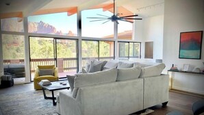 A spacious living room with a large white sofa, a yellow armchair, and a coffee table. There are large windows offering a view of the outdoors.