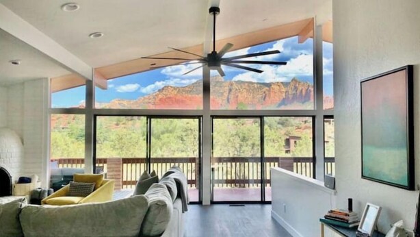 A spacious living room with a large window overlooking a mountainous landscape, a ceiling fan, and a modern fireplace.