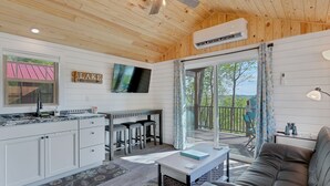 Interior d'una cabana amb cuina, zona de menjador i un balcó amb vistes als arbres.