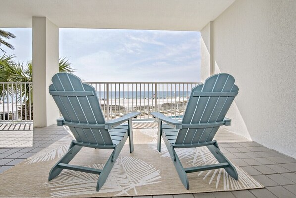 Two Adirondack chairs on a balcony with a view of the beach.
