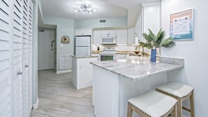 Una cocina moderna con armarios blancos, una isla central con taburetes, un microondas y un horno.