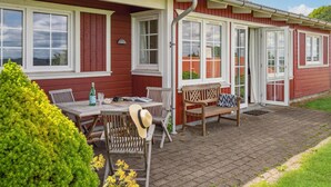 Ett rött trähus med vita detaljer, en uteplats med ett bord och stolar samt en liten trädgård.