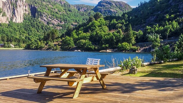 A wooden deck with a picnic table and benches overlooking a lake with mountains in the background. - Awesome home in Farsund with WiFi (Farsund)