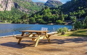 Una terrazza in legno con tavolo da picnic e panche che si affaccia su un lago con montagne sullo sfondo.