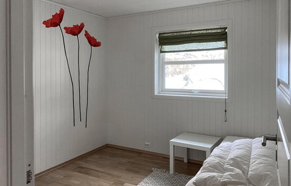 Camera da letto con un letto, un comodino, una finestra vista alberi e una parete con tre fiori rossi.