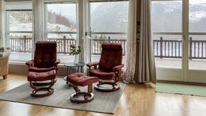 A cozy room with two rocking chairs and a small table with a vase of flowers, large windows with a view of a snowy landscape. - Awesome home in Farsund with WiFi (Farsund)