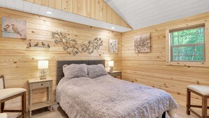 A cozy wooden cabin bedroom with a large bed, two bedside tables with lamps, a window with a view of trees, and wall art. - Lake View Nature Cabin at Bear Bluff Retreat (Walling)