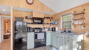 A modern kitchen with a stainless steel refrigerator, a microwave, and a stove. There is a window with a view of greenery outside. - Lake View Nature Cabin at Bear Bluff Retreat (Walling)