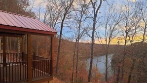 A wooden cabin with a metal roof overlooking a forested area with a lake. - Lake View Nature Cabin at Bear Bluff Retreat (Walling)