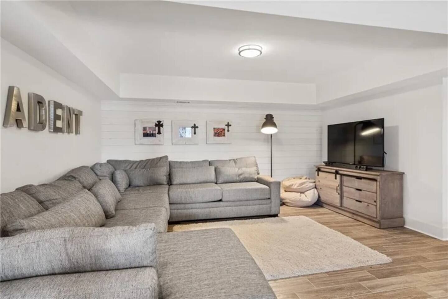 A living room with a sectional sofa, a flat-screen TV, a wooden cabinet, and a floor lamp.