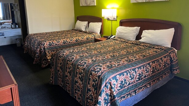 A hotel room with two beds, each with patterned bedding, a bedside table, a lamp, and artwork on the walls. - Lebanon Inn Motel (Lebanon)