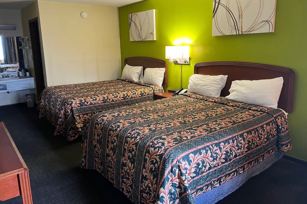 A hotel room with two beds, each with patterned bedding, a bedside table, a lamp, and artwork on the walls.