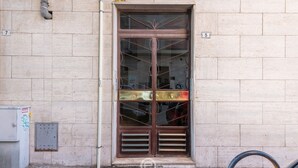 A building entrance with a large, ornate metal door, numbered 5 and 7, and a small utility box to the left. - Harbor View Apartment (Cagliari)