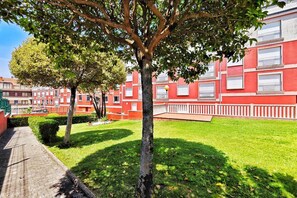 A courtyard with a tree, a red building with balconies, and a paved walkway. - Disconnectaengalicia La Perla Premium, swimming pool and parking (Portonovo)