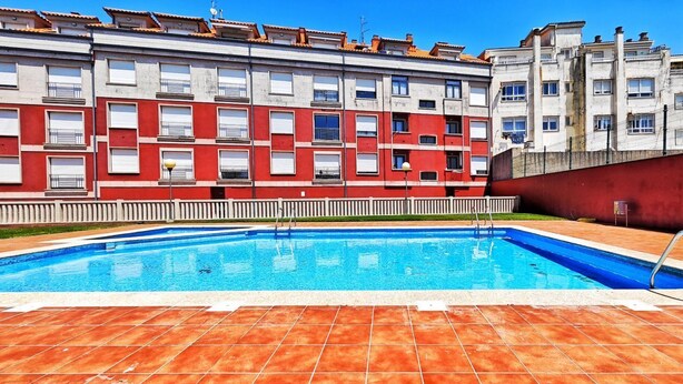 Une piscine dotée d’une terrasse carrelée, entourée d’un bâtiment aux murs rouges et blancs et aux nombreuses fenêtres.