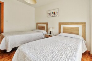 A hotel room with two beds, wooden headboards, a nightstand with a lamp, and a wall-mounted picture.