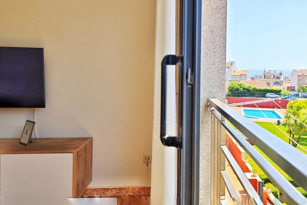 A balcony with a pool view, a TV mounted on the wall, and a wooden side table with a picture frame.
