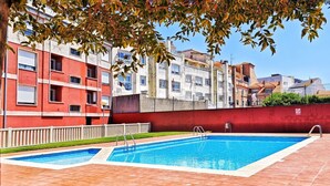 A swimming pool with two ladders, surrounded by a red wall and a white fence, with buildings in the background. - Disconnectaengalicia La Perla Premium, swimming pool and parking (Portonovo)