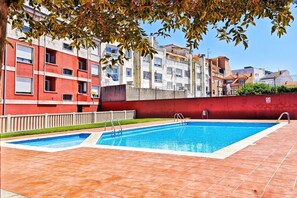Una piscina amb dues escales, envoltada per un mur vermell i una tanca blanca, amb edificis al fons.