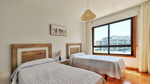 A hotel room with two beds, a large window with a city view, a hanging light fixture, and a framed picture on the wall. - Disconnectaengalicia La Perla Premium, swimming pool and parking (Portonovo)