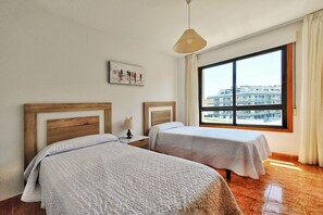 Habitació d'hotel amb dos llits, una finestra gran amb vista a la ciutat, una làmpada penjant i un quadre al mur.